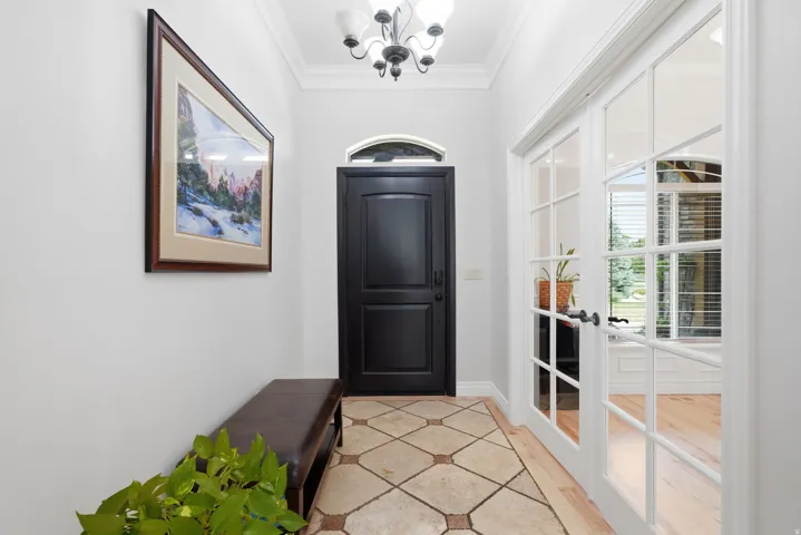 Arched transom above the entry door, travertine flooring, chandelier lighting, crown molding, and French doors with grid-patterned glass
