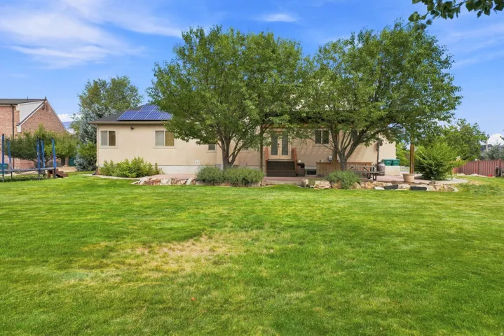 Expansive backyard featuring a manicured lawn, established trees.