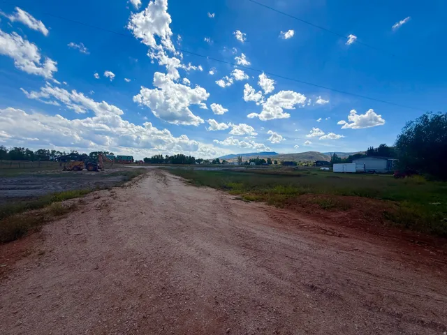 Expansive open land featuring a dirt road, distant residential structures, and natural vegetation