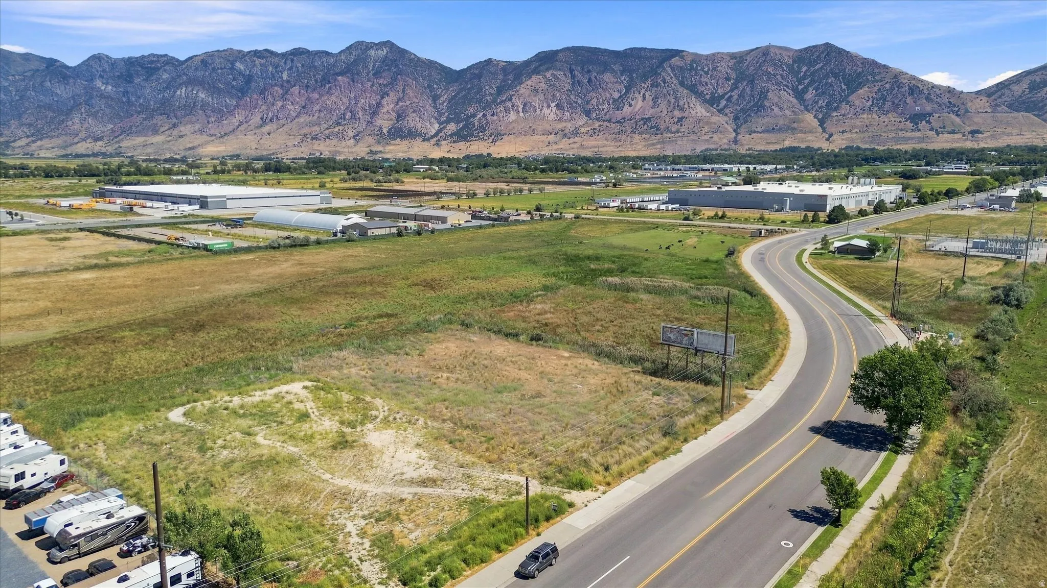 Expansive undeveloped land with a paved road, surrounded by natural terrain and distant mountains