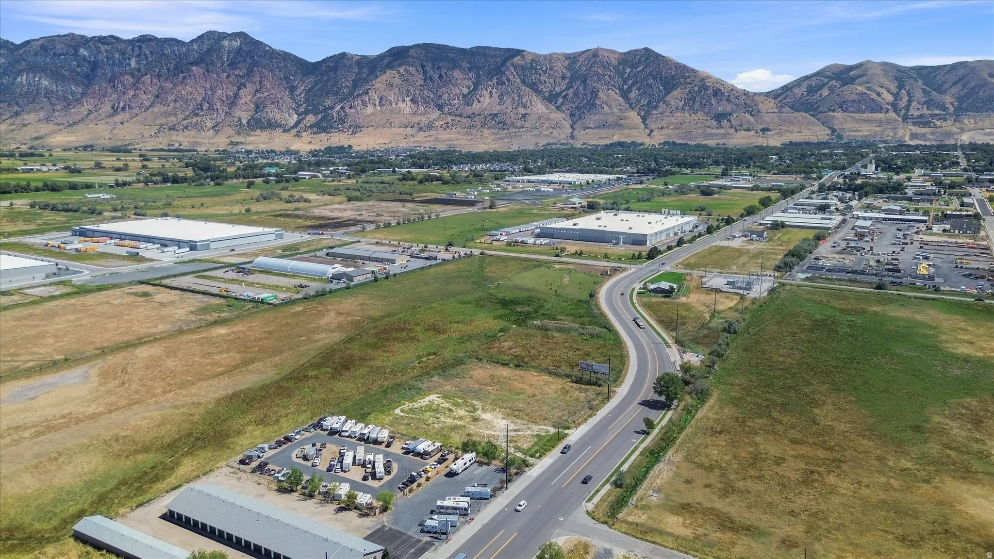Expansive undeveloped land featuring a paved road, mountain backdrop, and commercial structures