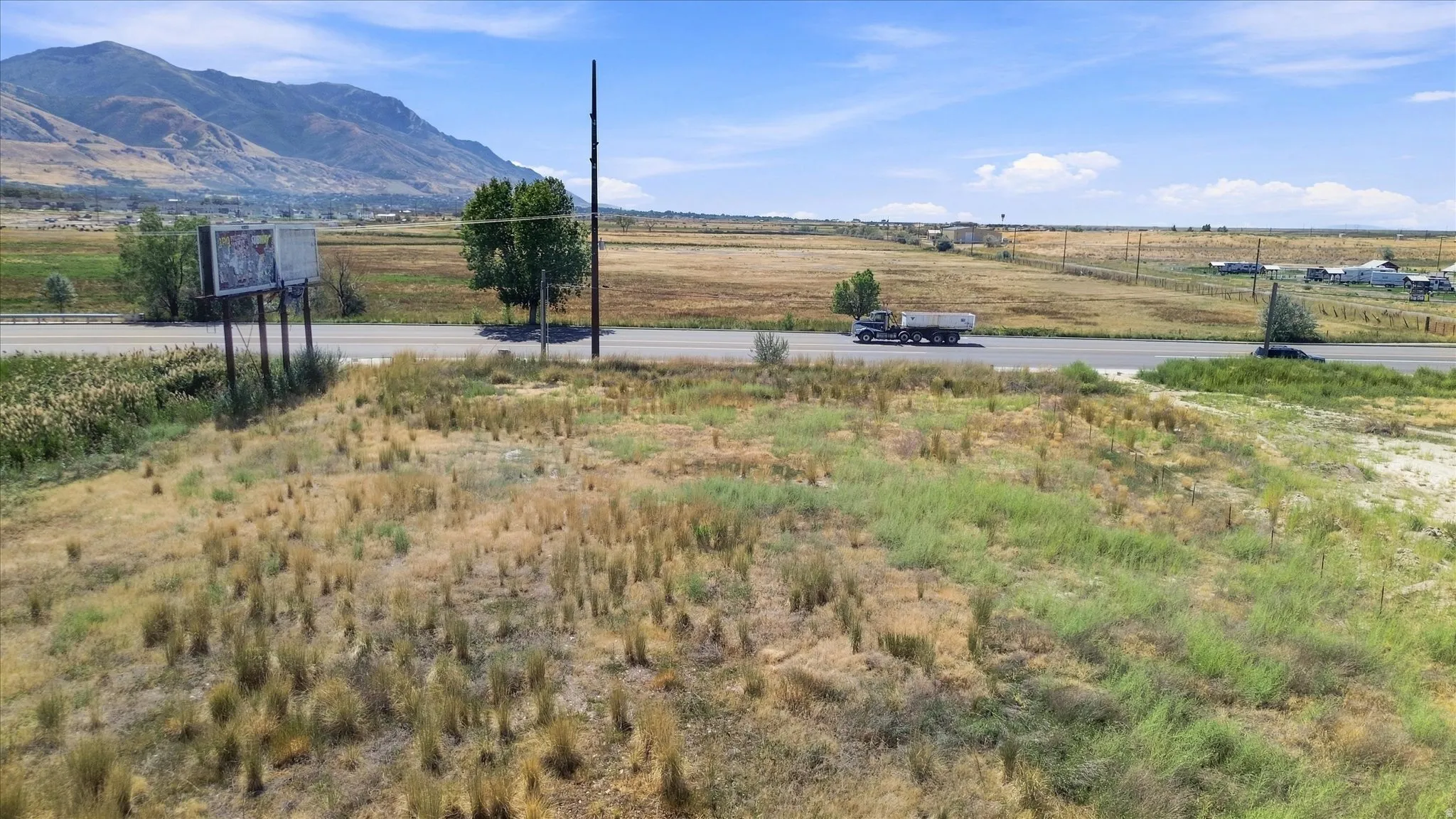 Expansive undeveloped land featuring a paved road, mountain backdrop, and natural vegetation