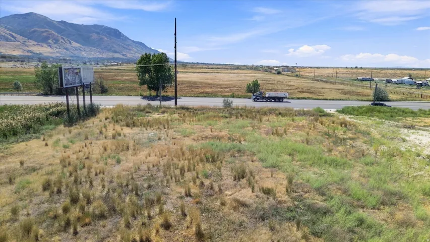 Expansive undeveloped land featuring a paved road, mountain backdrop, and natural vegetation