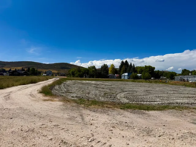 Expansive undeveloped lot with a dirt road access, surrounded by distant hills and natural landscaping