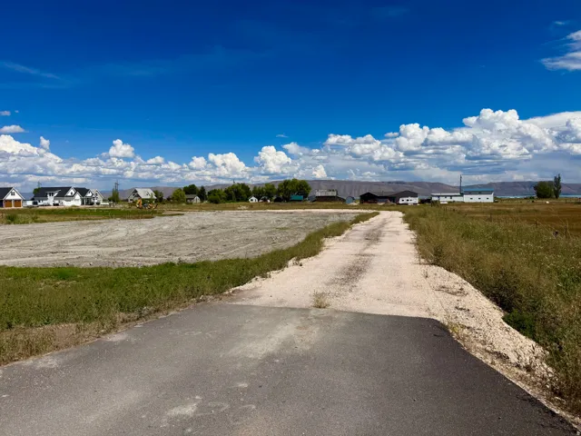 Paved and gravel drive, cultivated land, distant structures, and open sky