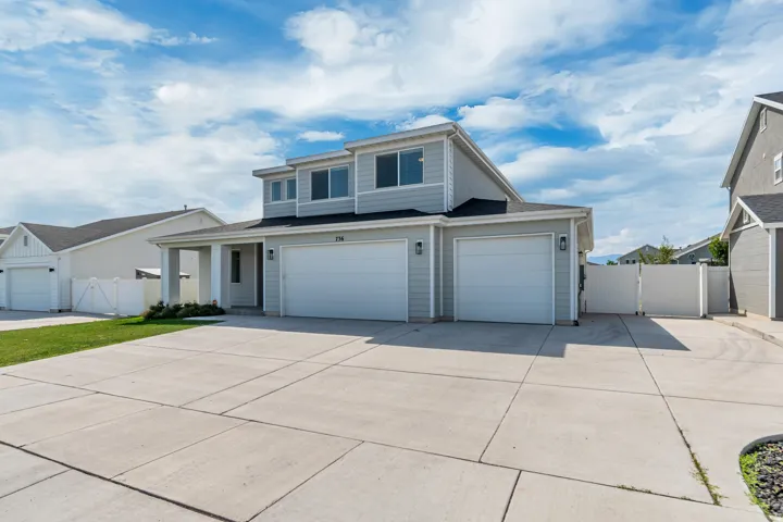 Two-story residence with a gray siding exterior, featuring two attached garages with white doors, a concrete driveway, and a covered entry porch