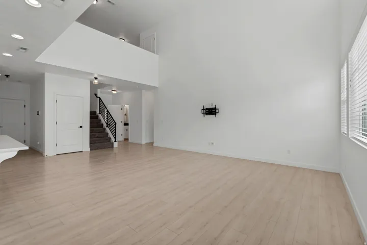 High ceilings with recessed lighting, light wood-finish flooring, staircase with dark handrails, and upper-level balcony