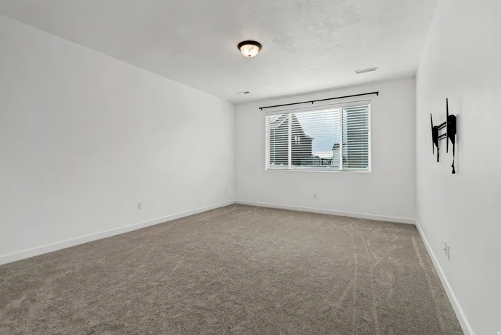 Bright secondary bedroom featuring neutral carpet flooring, white walls, and a large window with louvered shutters providing natural light