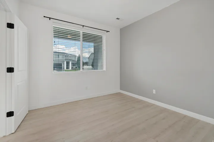 Light wood-finish flooring, white walls, and a single window with blinds