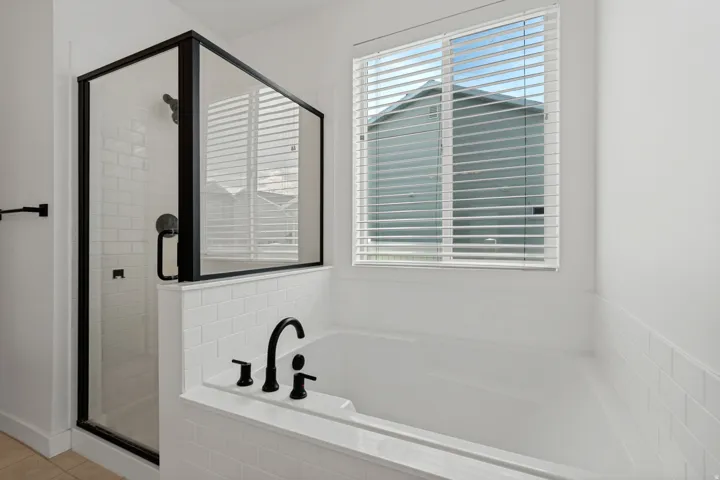Built-in bathtub with black fixtures, subway tile surround, and a clear glass shower enclosure with black framing