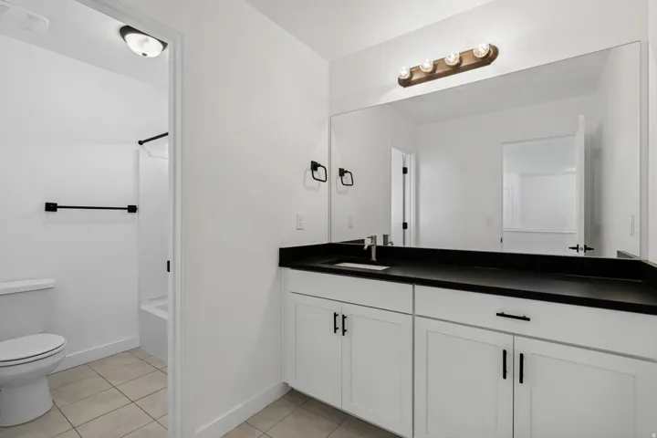 White vanity with dark countertop, large wall-mounted mirror, and tile flooring