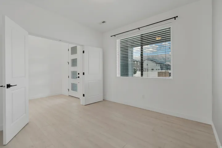 Light wood-finish flooring, white walls, and a large window with white blinds