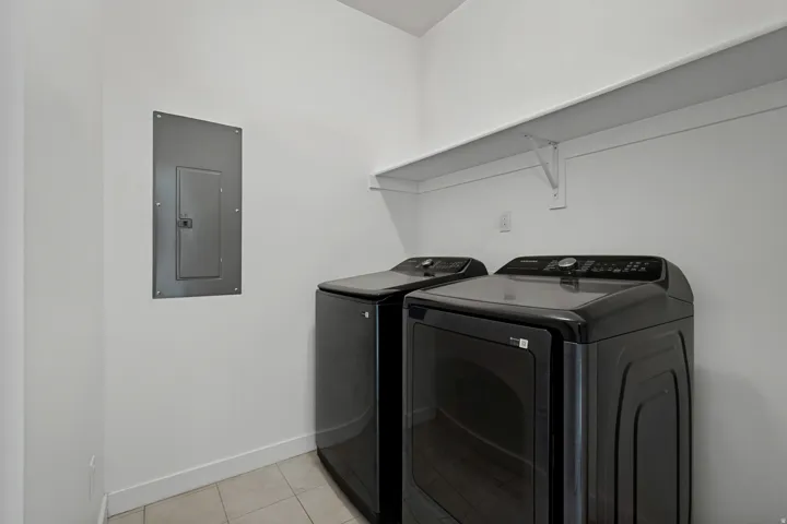 Built-in laundry appliances, overhead shelving, and tile flooring