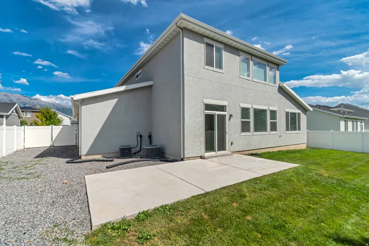 Rear exterior with a concrete patio, sliding glass door, multiple windows, and a grassy lawn