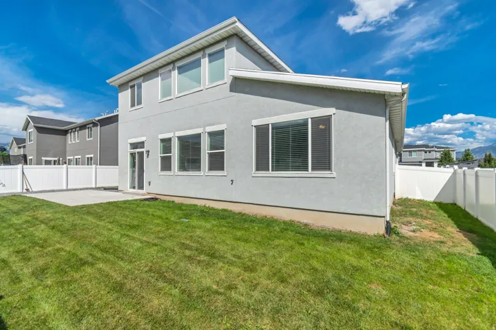 Expansive backyard featuring a manicured lawn, concrete patio, and white privacy fencing