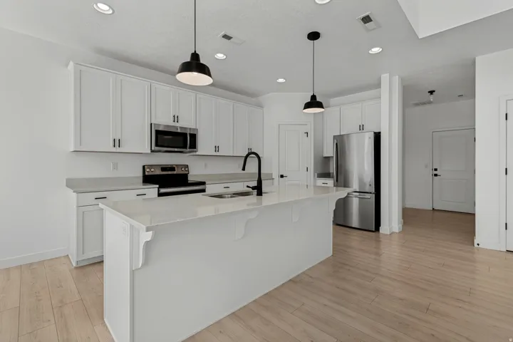 Modern kitchen featuring white cabinetry, stainless steel appliances, a center island with sink, black pendant lighting, and wood-finish flooring