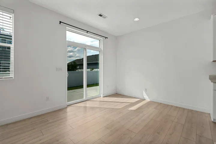 Bright, open room featuring pristine wood-finish flooring, recessed ceiling lighting, and sliding glass doors with black framing that flood the space with natural light