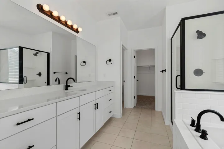 Dual vanity with white cabinetry and integrated sinks, matte black fixtures, framed glass shower, and soaking tub with subway tile surround