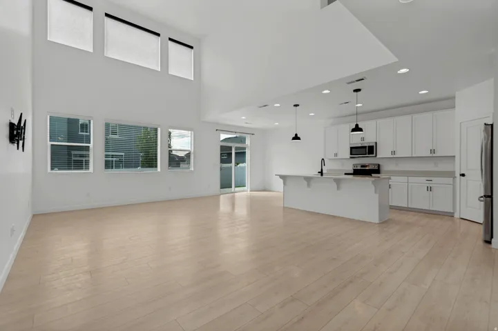 High ceilings, wood-finish flooring, white cabinetry, kitchen island with sink, and recessed lighting