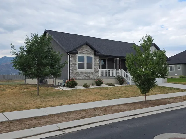 Charming stone-front cottage with a welcoming covered front porch, dark asphalt shingle roof, and contemporary window styling