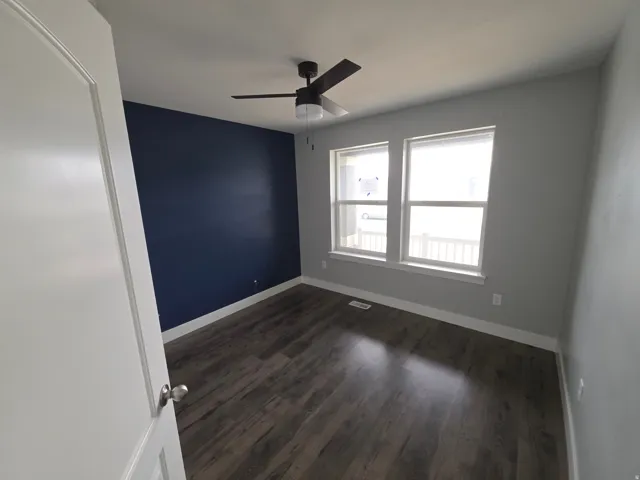 Wood-finish flooring, two large windows, accent wall, ceiling fan with light fixture