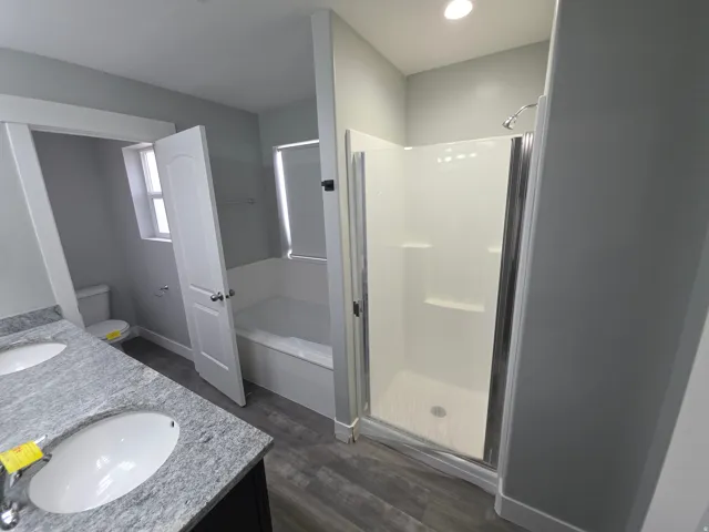 Double vanity with stone-finish countertop, wood-finish flooring, built-in bathtub, and enclosed shower with glass door