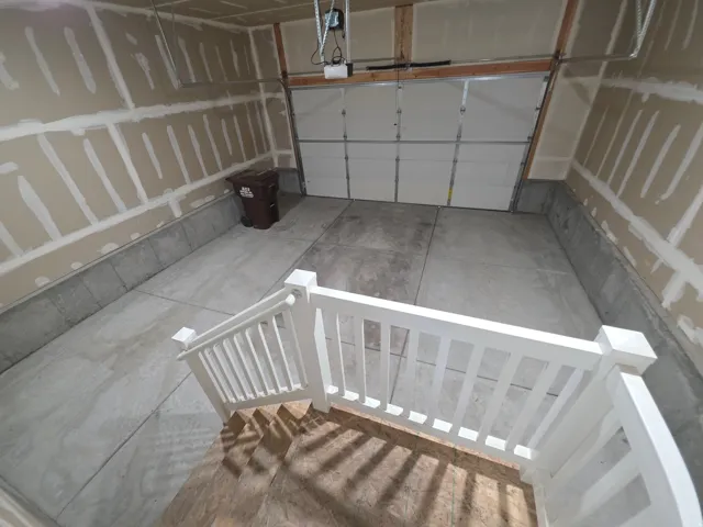Concrete flooring, exposed stud walls, automatic garage door system, white painted railing, partially finished walls