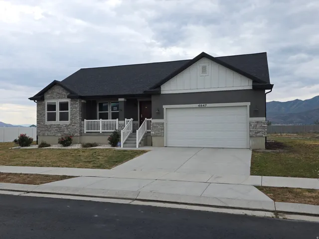 Single-story residence featuring a dark gray exterior with stone accents, a dark shingle roof, a front porch with white railing, and an attached two-car garage