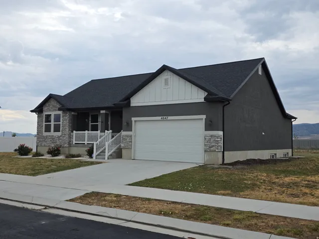 Stone facade accents, concrete driveway, covered porch with white railings, dark gray exterior siding, and a two-car garage