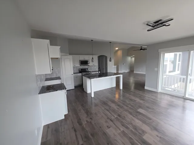 Spacious kitchen featuring white cabinetry, dark stone countertops, stainless steel appliances, and a tiled backsplash
