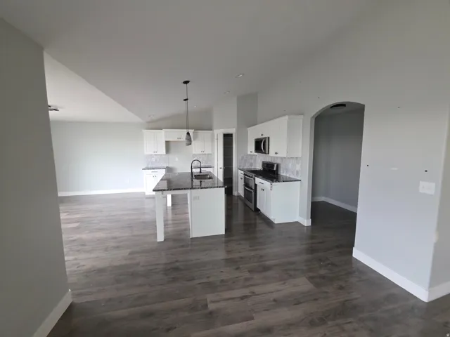 Open-concept kitchen featuring white cabinetry, dark countertops, a tile backsplash, and stainless steel appliances