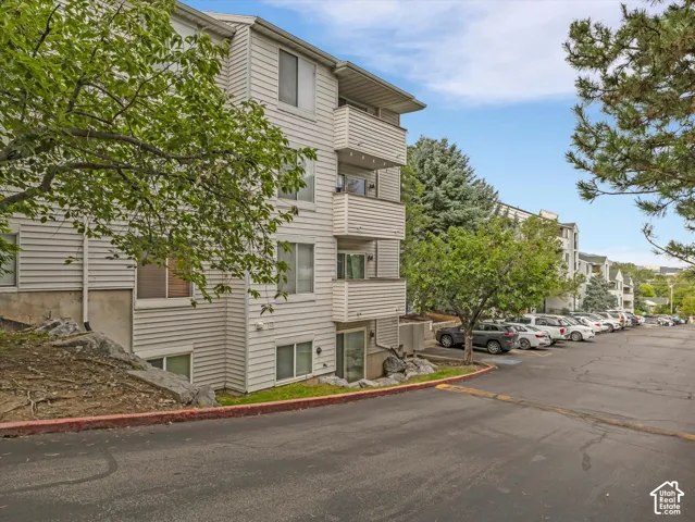Multi-story building featuring horizontal siding, multiple balconies, and an adjacent asphalt parking area