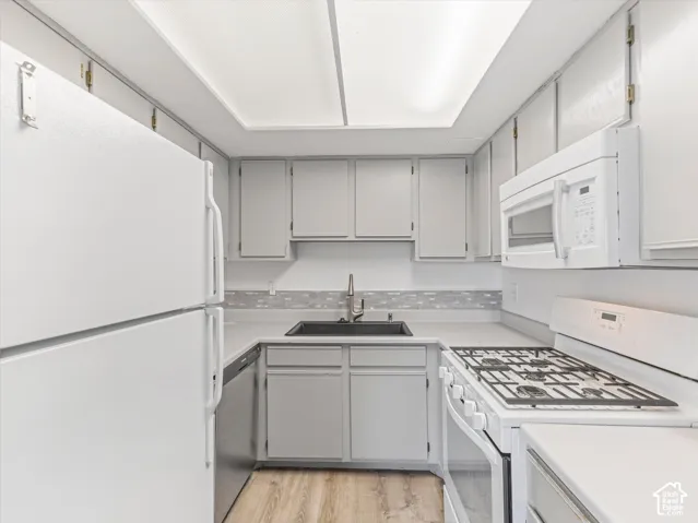Kitchen featuring light gray cabinetry, white appliances, a black sink, and light wood-finish flooring