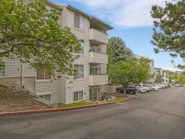 Multi-story building featuring horizontal siding, multiple balconies, and an adjacent asphalt parking area