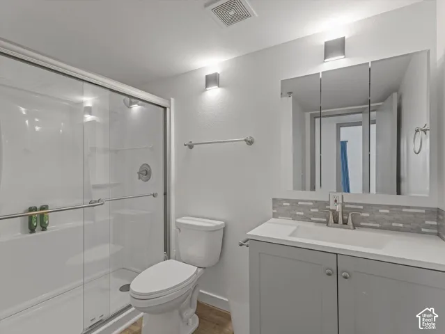 Enclosed shower with sliding glass doors, contemporary vanity with integrated sink, modern medicine cabinet, and mosaic tile backsplash