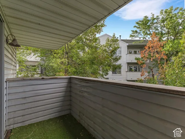 Balcony with horizontal siding, a textured ceiling, a wall-mounted light fixture, and artificial turf flooring