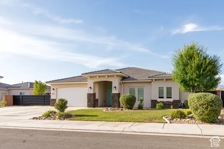 Stucco exterior with stone accents, a covered entry, an attached garage, and a manicured lawn