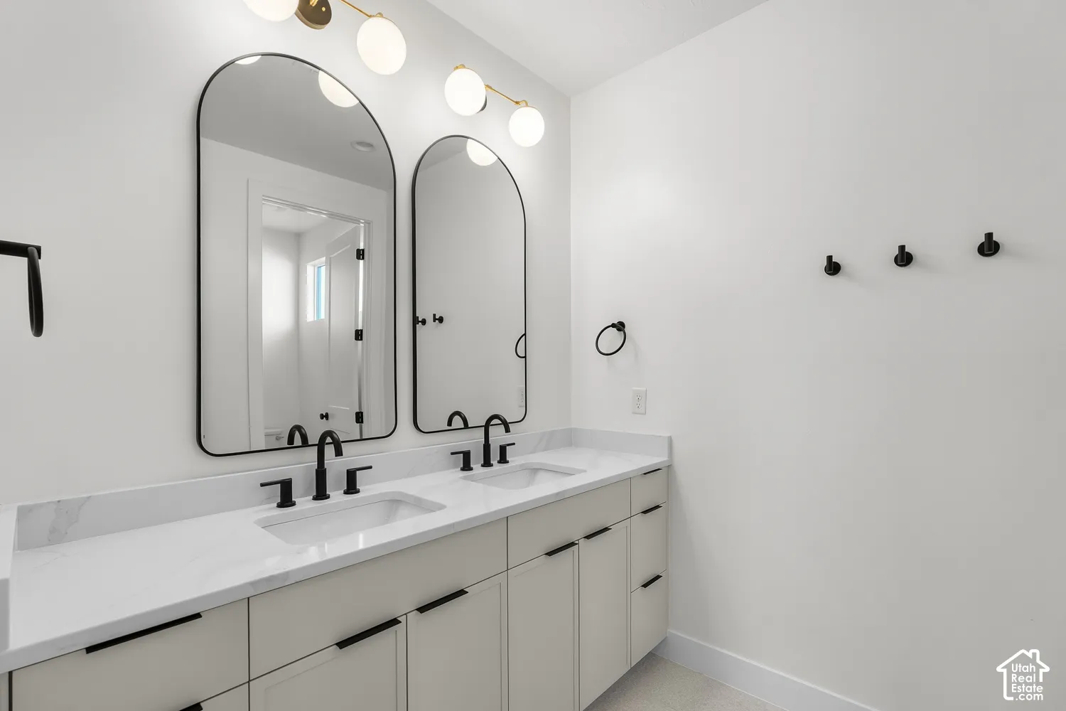 Double vanity with white countertops, matte black fixtures, arched mirrors, and a multi-bulb light fixture
