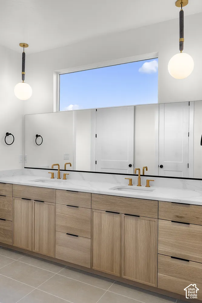Dual vanities with integrated sinks, light wood-finish cabinetry, a large transom window, and contemporary pendant lighting
