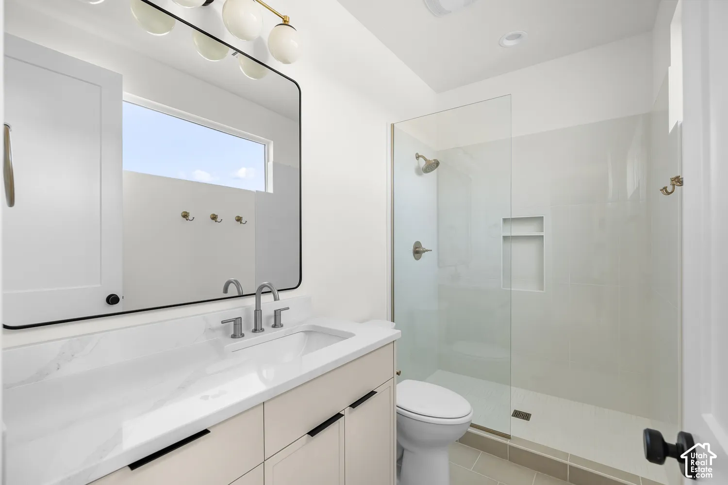 Neutral-toned vanity with a white countertop and undermount sink, brushed nickel faucet, and a frameless glass shower enclosure with a built-in niche