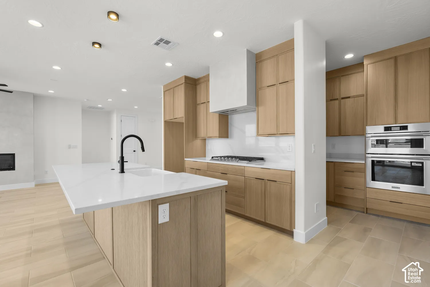 Kitchen featuring a large island with white countertops, light wood-finish cabinetry, stainless steel double ovens, and a gas range