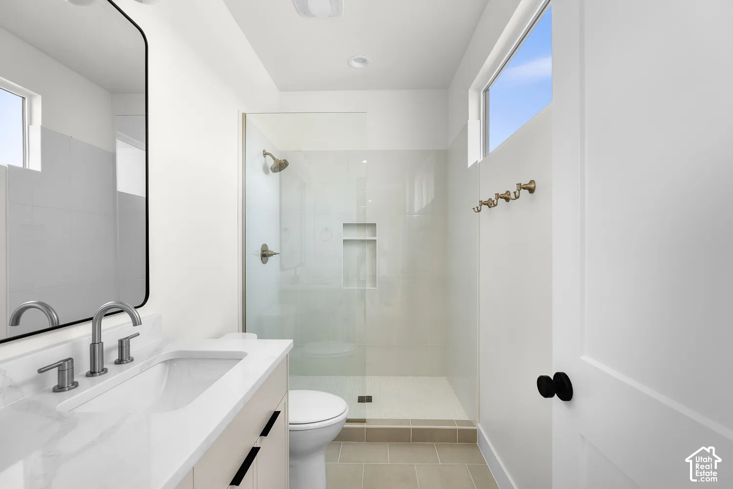 Bathroom featuring a floating vanity with a white countertop and rectangular sink, a glass-enclosed shower with a built-in niche, and a transom window