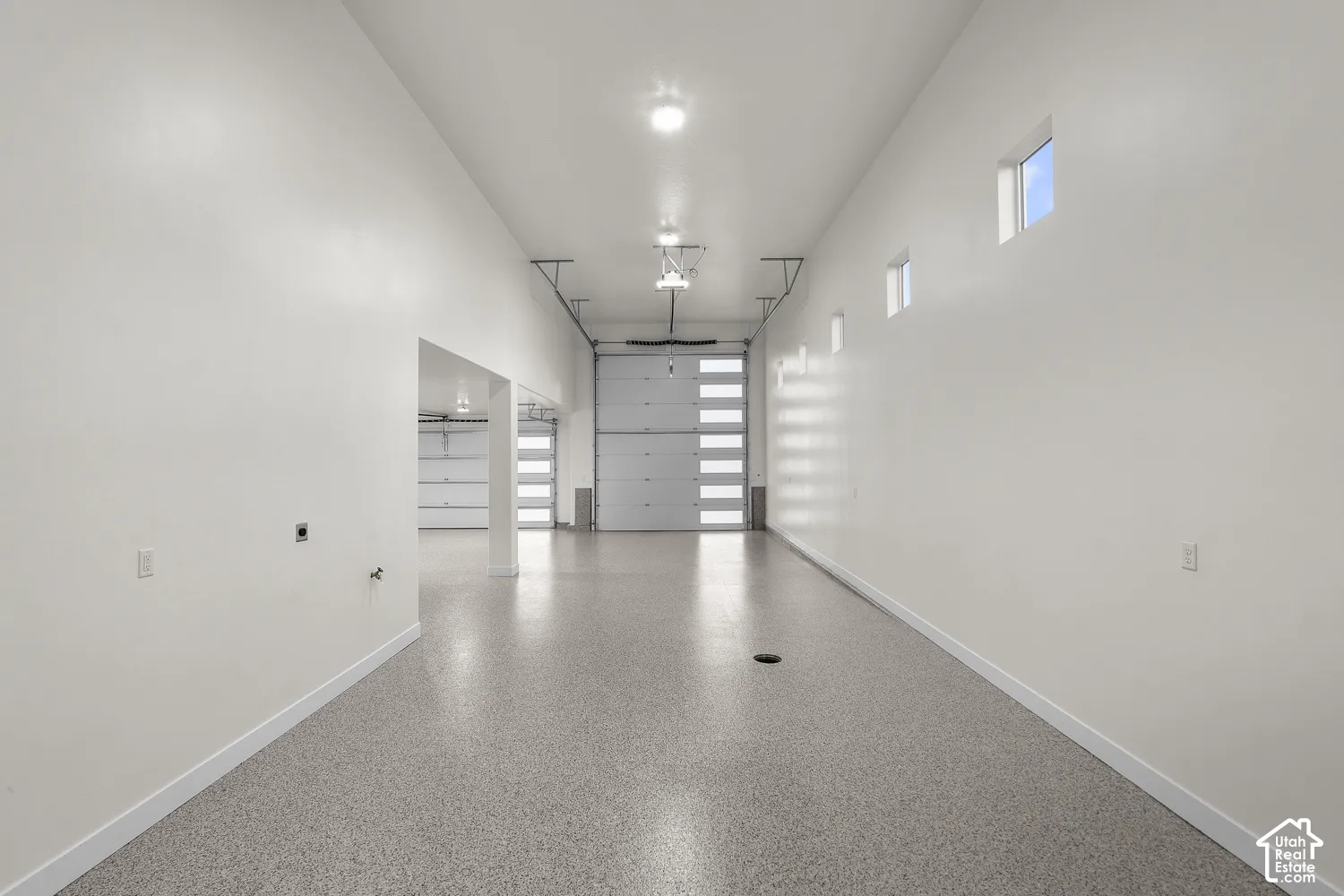 Spacious garage interior featuring polished concrete flooring, abundant natural light from clerestory windows, overhead recessed lighting, and multiple wall-mounted storage shelving units