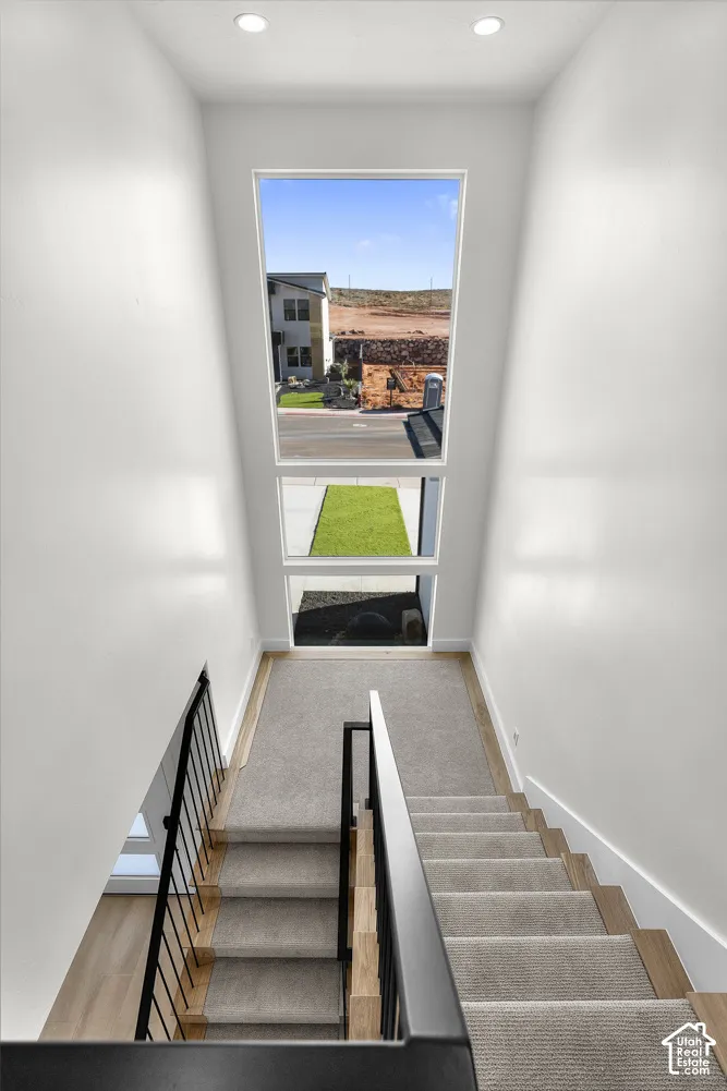Stairwell featuring carpeted treads, wood-finish risers, and black metal railings