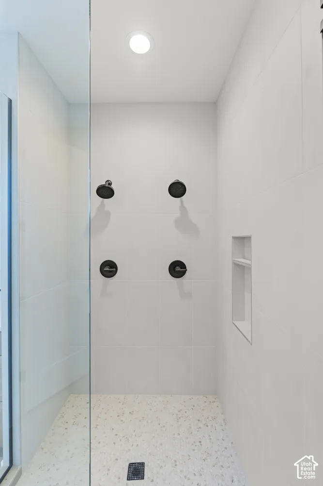 Glass-enclosed shower featuring dual matte black showerheads, integrated niche shelving, white tile walls, and a speckled floor