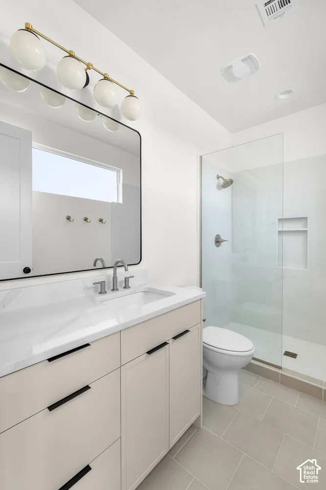 Bathroom featuring a single vanity with stone-finish countertop, frameless shower enclosure, and tiled flooring