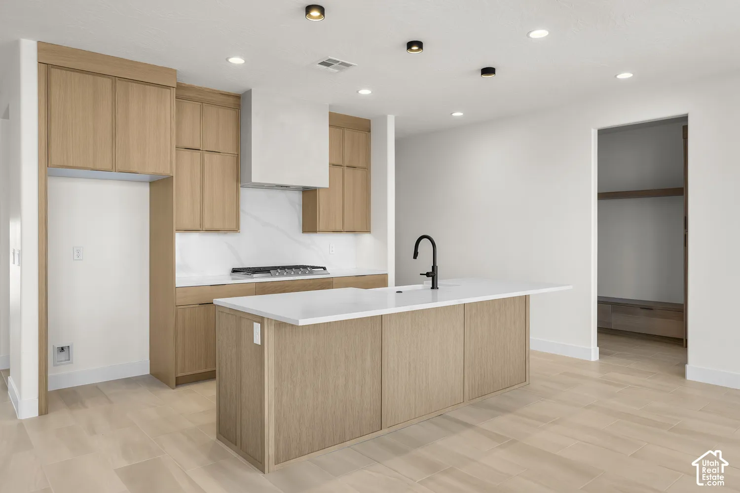 Kitchen featuring wood-finish cabinetry, a large center island with a white countertop and integrated sink, a built-in range, and white tiled backsplash