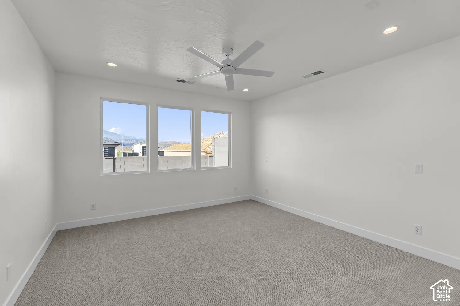Spacious room featuring three large windows, recessed ceiling lighting, a ceiling fan, and light-colored carpeting
