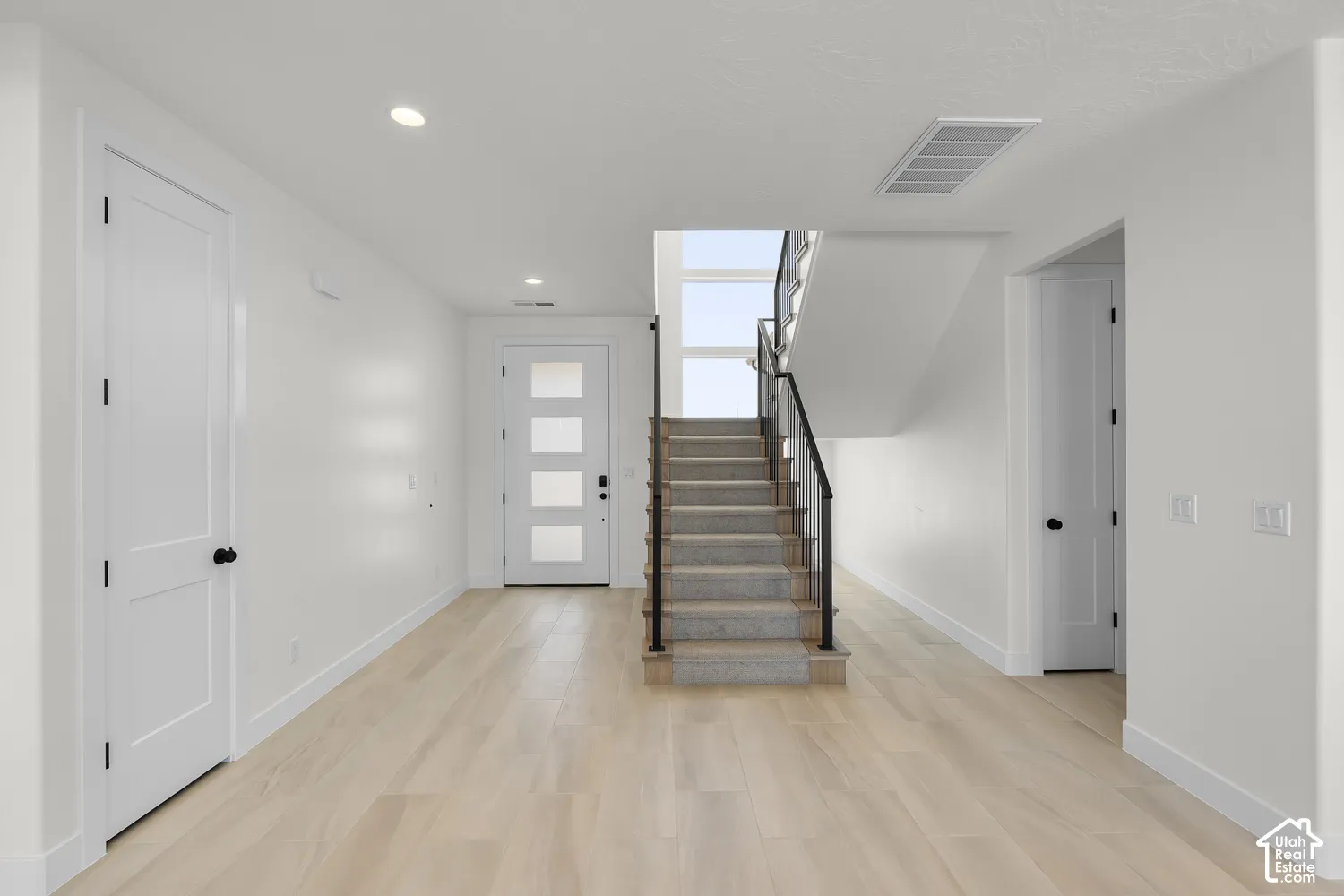 Light wood-finish flooring, recessed ceiling lighting, a contemporary staircase with metal railings, and a front entry door with frosted glass panels