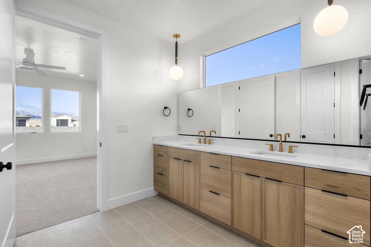 Double vanity with light wood finish cabinetry, gold-tone fixtures, and white countertop